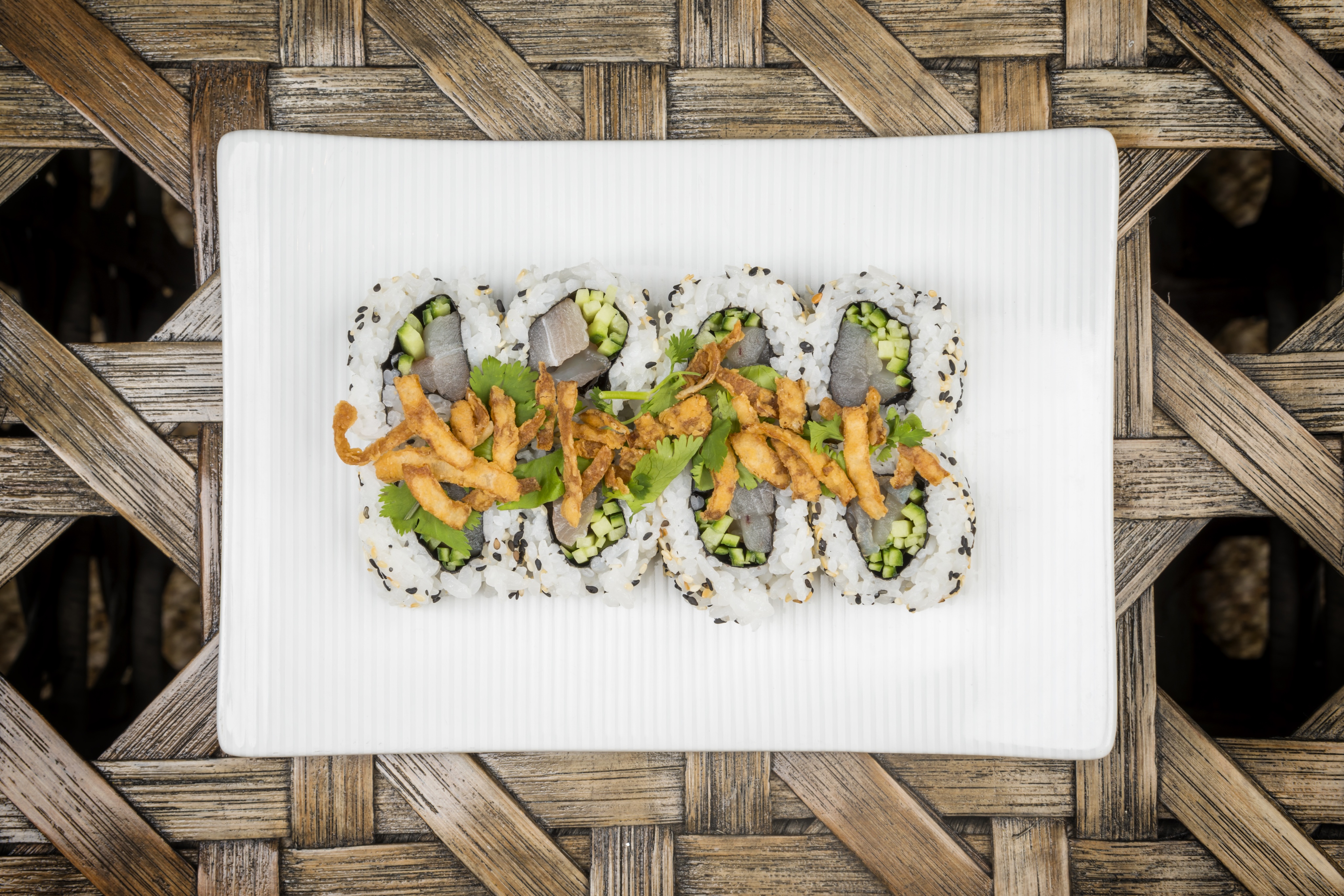 A gallery-worthy plate of sushi rolls topped with avocado slices and crispy fried onions, served on a white rectangular dish.