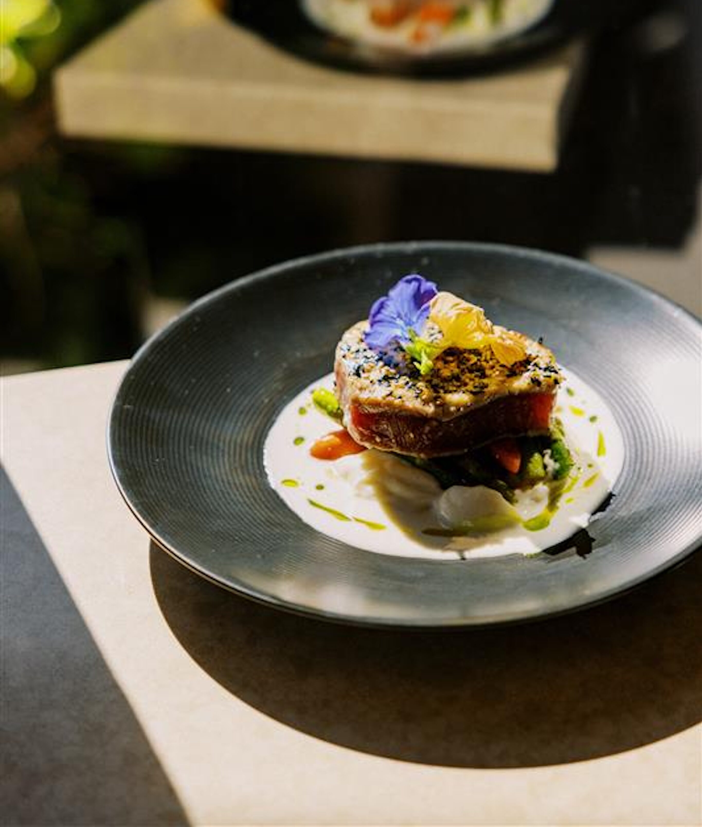 A plated gourmet dish featuring a seared piece of fish garnished with edible flowers and sauce, its reflection shimmering nearby—perfectly crafted for memorable celebrations.