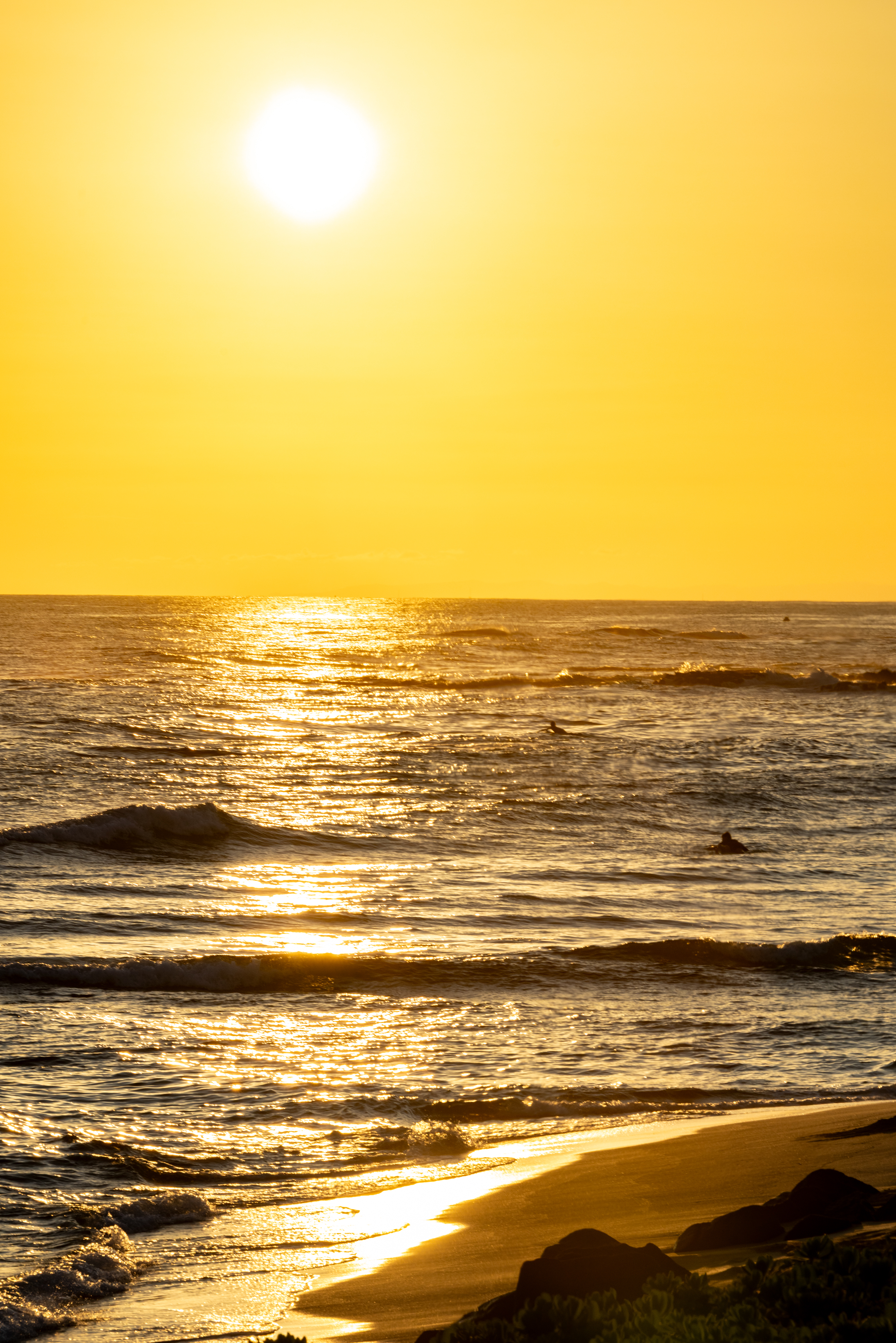 The sun sets over the ocean, casting a golden glow on the waves and sandy shoreline.