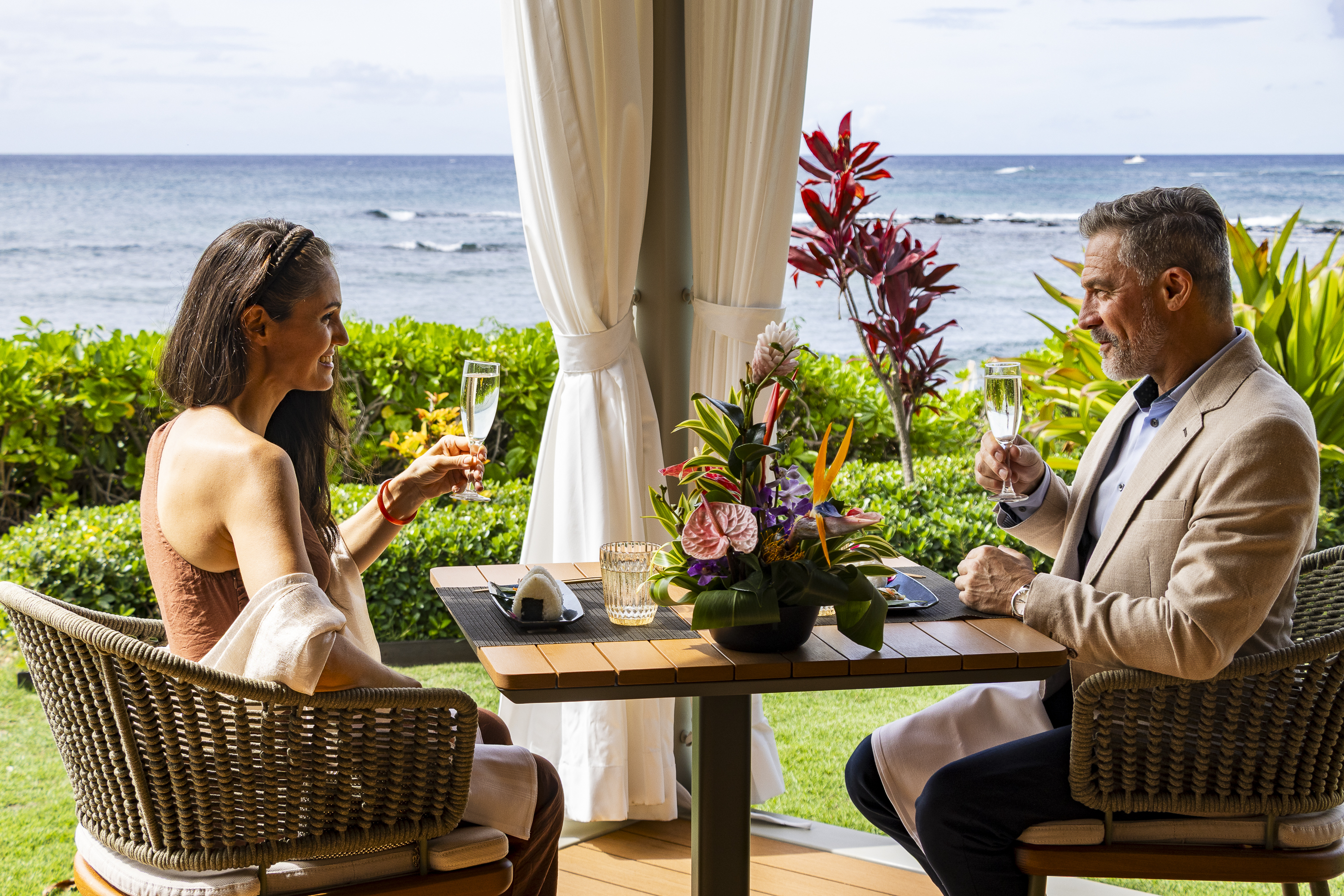 A man and woman sit at a table with drinks, enjoying an evening reminiscent of cozy Cabana Dinners.